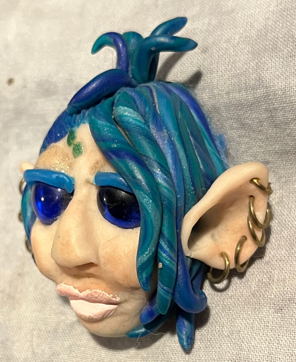 TeWana Asteria sculpted brooch, side view showing blue-green hair and pierced ear